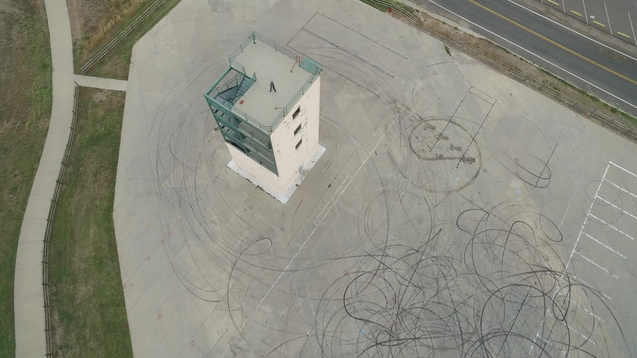 Overhead view of a white structure on a concrete lot with tire marks and a road edge.