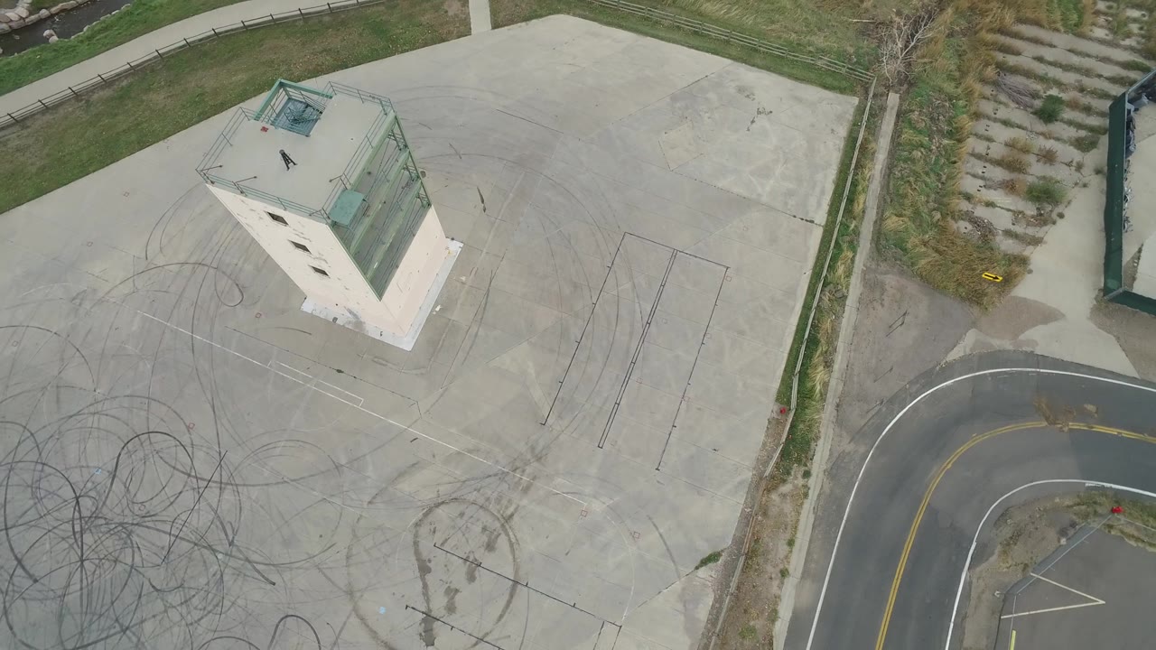 Top-down frame of building, concrete lot, road curve, and dense tire marks.