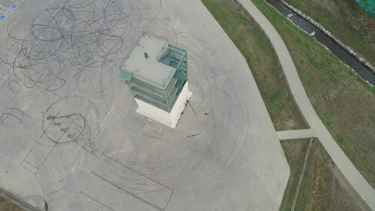 Overhead view of concrete lot, glass-topped structure, sidewalks, grass, and drainage channel.