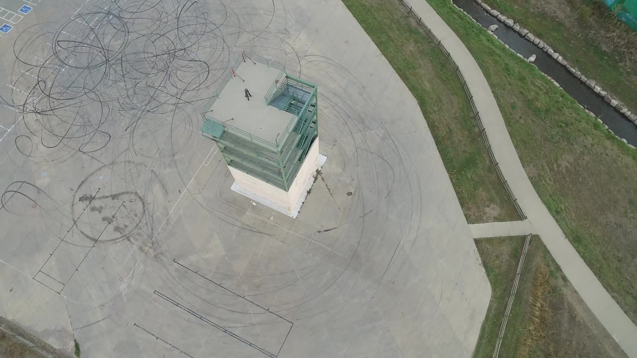 Hidden Lake, Colorado aerial frame with the glass-topped building element nearer the right side, broad concrete pavement covered in tire arcs, grass bands, sidewalks, and no clearly visible people.
