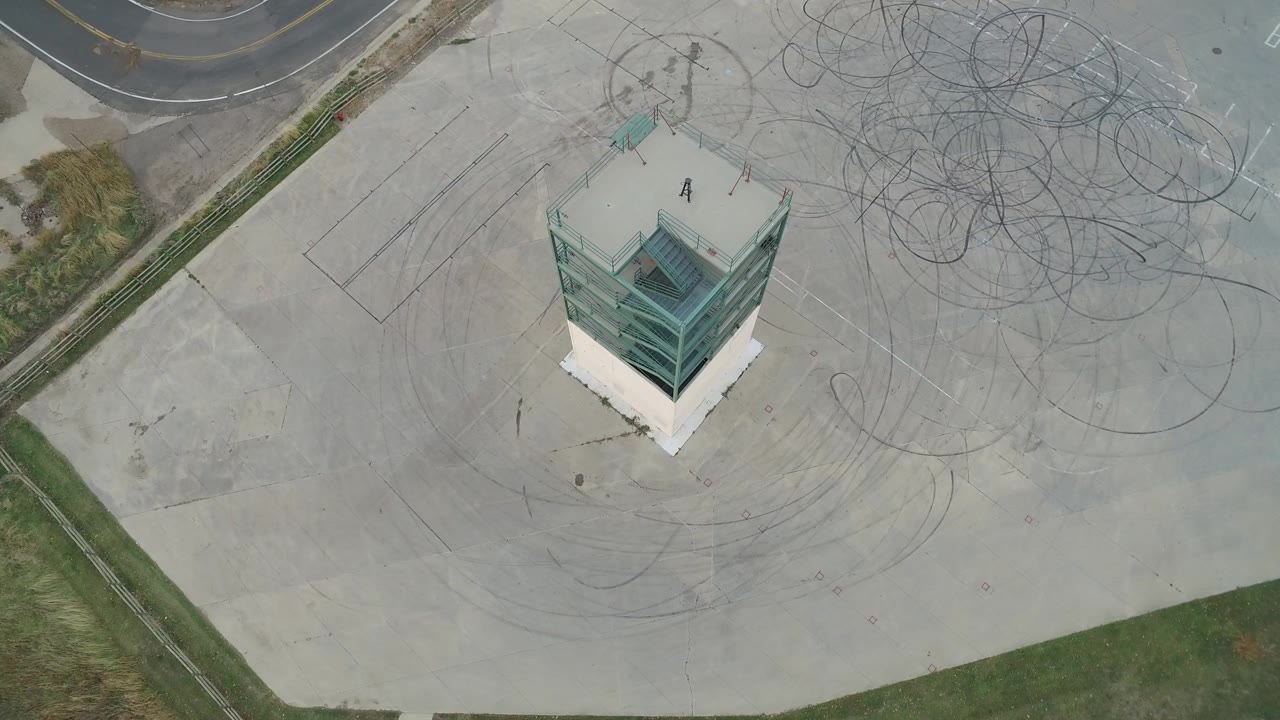 Top-down shot of a small structure beside large dark tire marks on concrete.