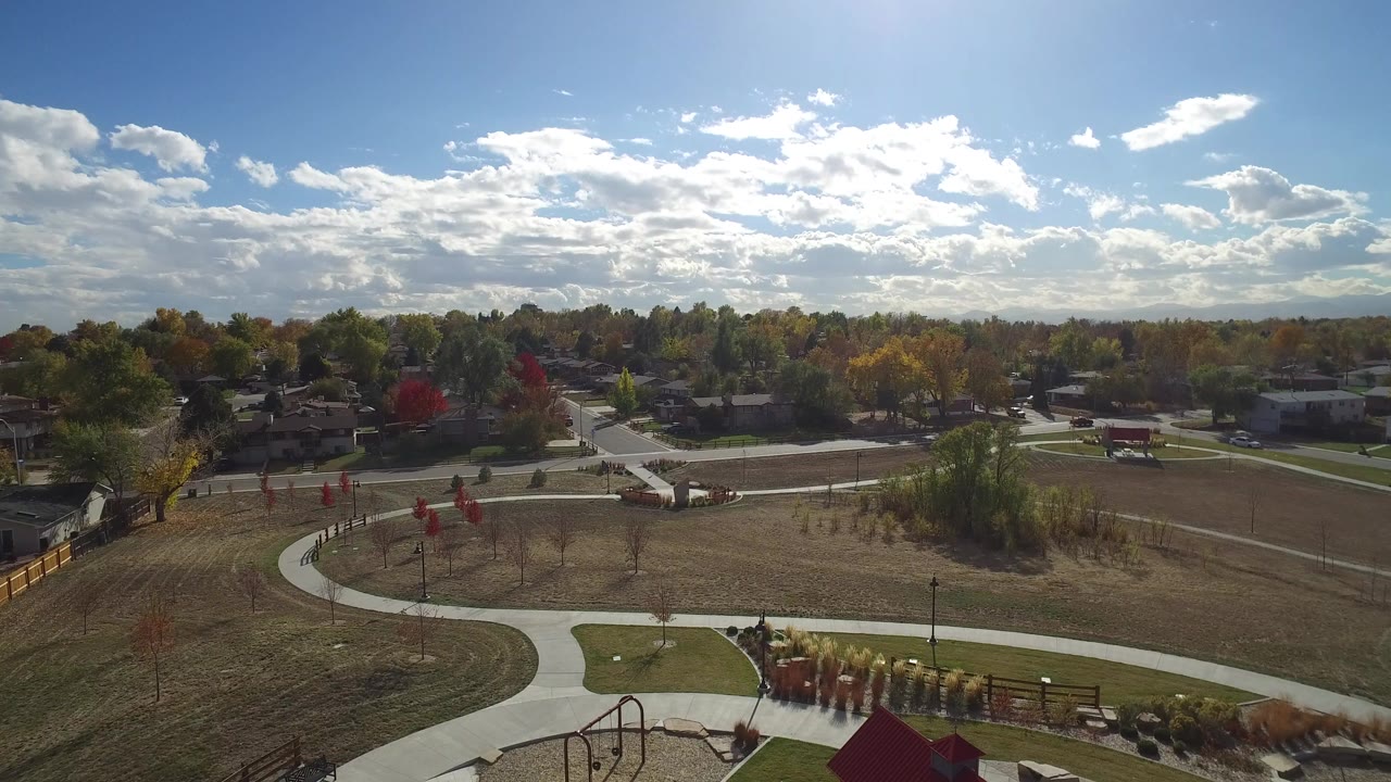 Opening aerial frame of a Hidden Lake, Colorado park with curving paved walkways, dry grass areas, neighborhood homes beyond the trees, and no visible people.