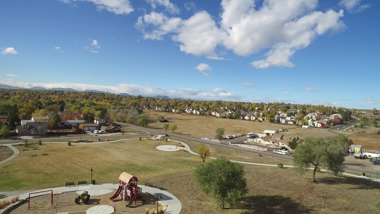 Early frame in Hidden Lake, Colorado, with the playground still low in frame, a circular paved area near the grass, roads beyond it, clustered homes, and no visible people.
