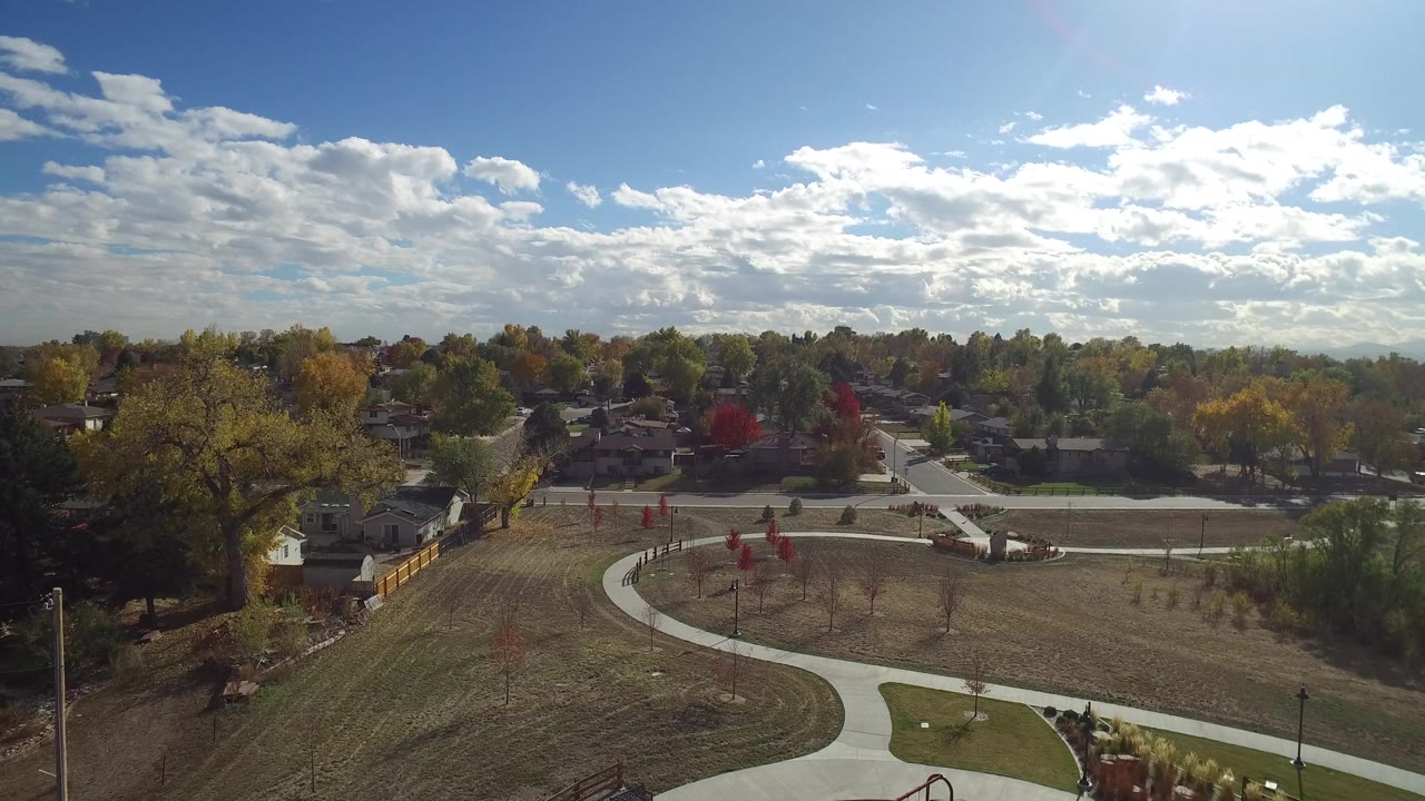 Elevated view of the Hidden Lake park as the path curve leads toward small planted trees, residential streets, houses, and a bright cloud-filled sky with no visible people.