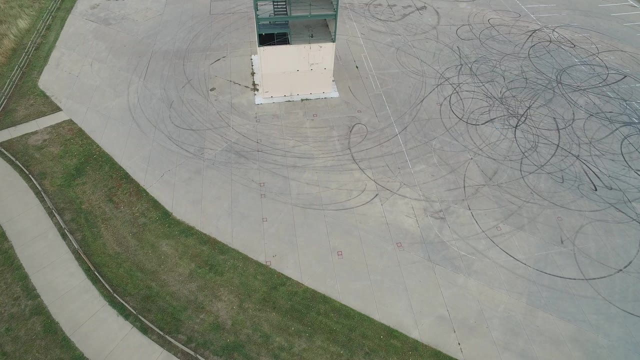 Aerial view of a concrete lot with skid marks, grass, path, and part of a building.