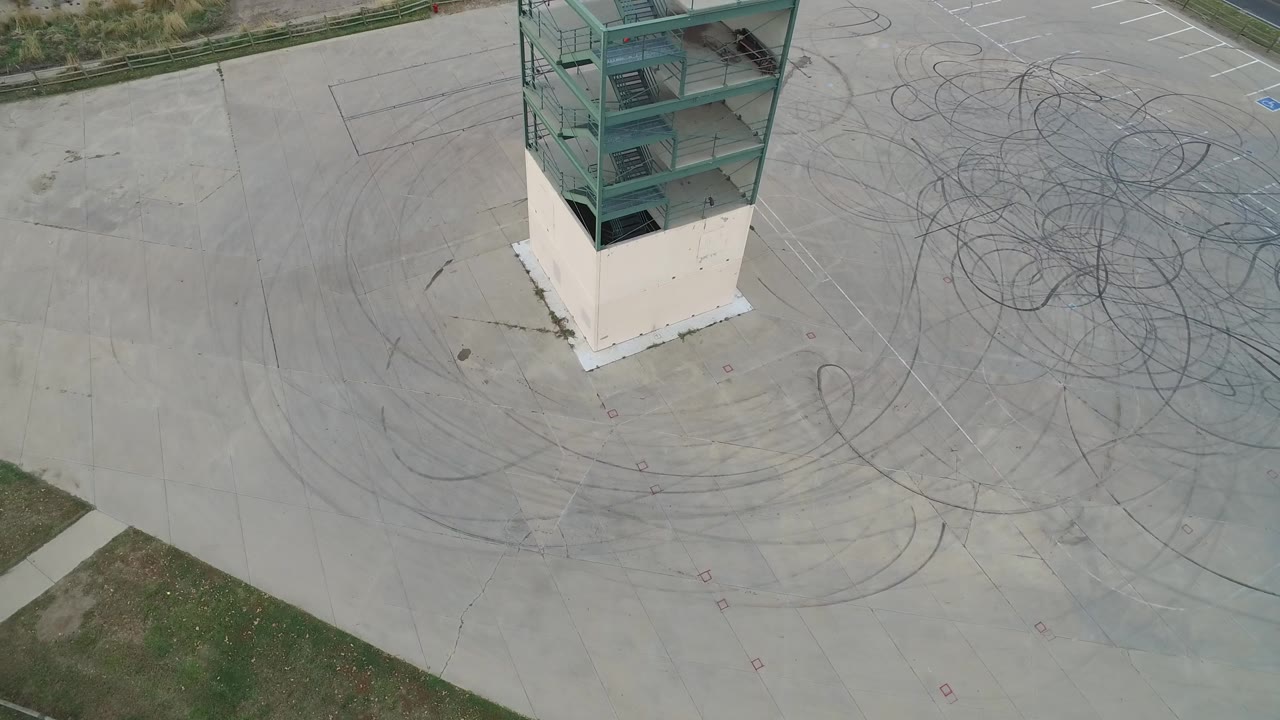 Aerial frame in Hidden Lake, Colorado with the green ramp structure near the upper left, a white base below it, looping tire marks across the concrete, grass along the edge, and no clearly visible person.