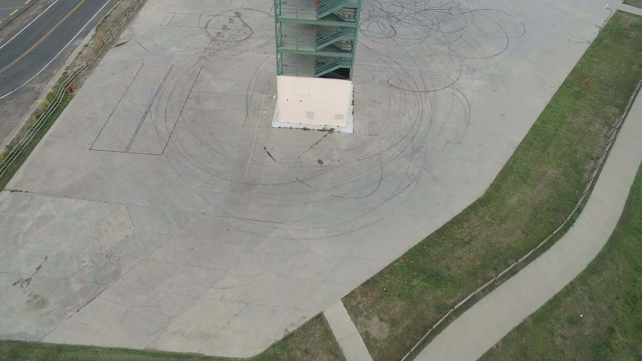 Overhead view of a concrete lot beside grass and a road edge.