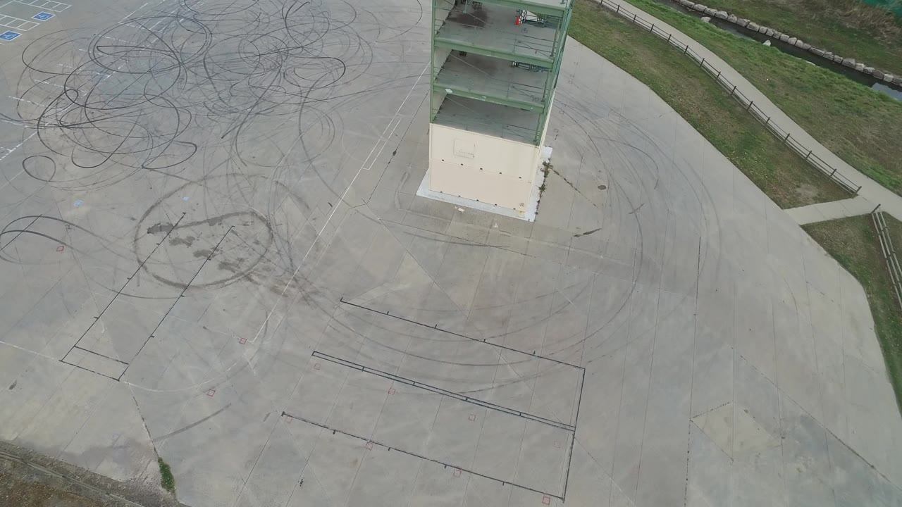 Aerial frame from Hidden Lake, Colorado showing a pale concrete construction area with looping tire marks, floor outlines, grass edges, and a green-column building structure, with no visible people.