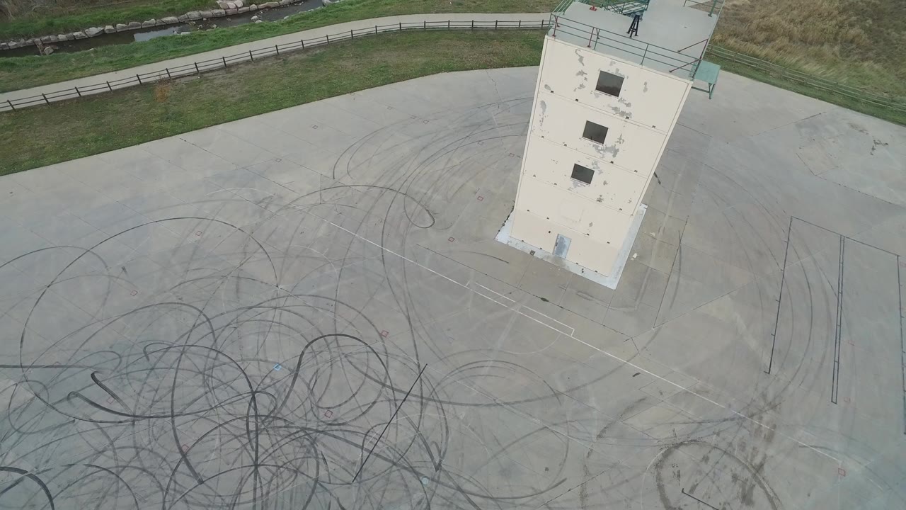 At 0:00, an overhead view at Hidden Lake Colorado shows a pale concrete pad crossed by dark tire arcs, with a tall white structure near the upper edge and no visible people.