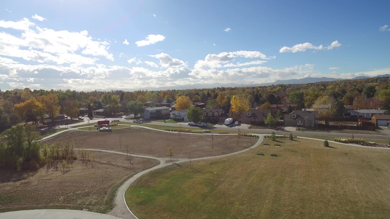 Aerial view of a park trail, open lawn, autumn trees, homes, and distant hills.