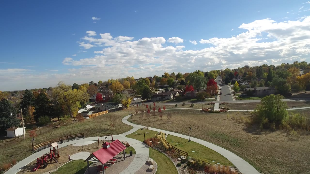 Aerial view of park paths, red shelter, playground, open field, trees, and houses.