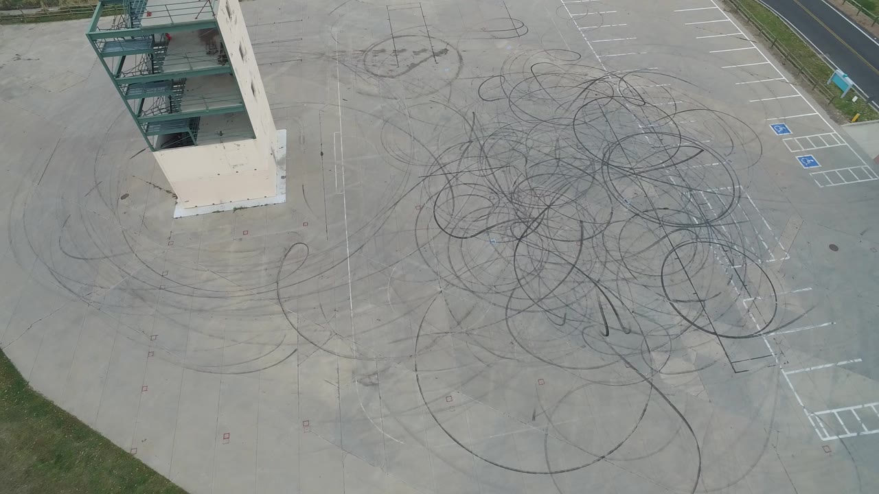 Overhead parking lot with circular tire marks and a building edge.