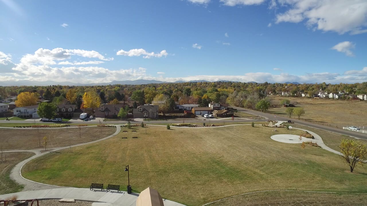Elevated view over grass, paths, benches, roads, houses, trees, and distant hills.