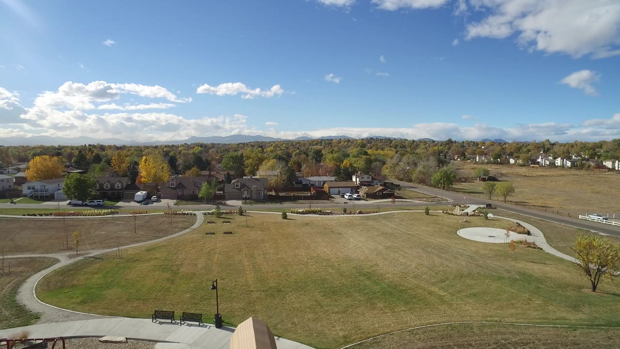 Hidden Lake, Colorado aerial frame with tan-green grass, intersecting paths, a road, residential buildings, yellow autumn trees, distant hills, and no visible people.