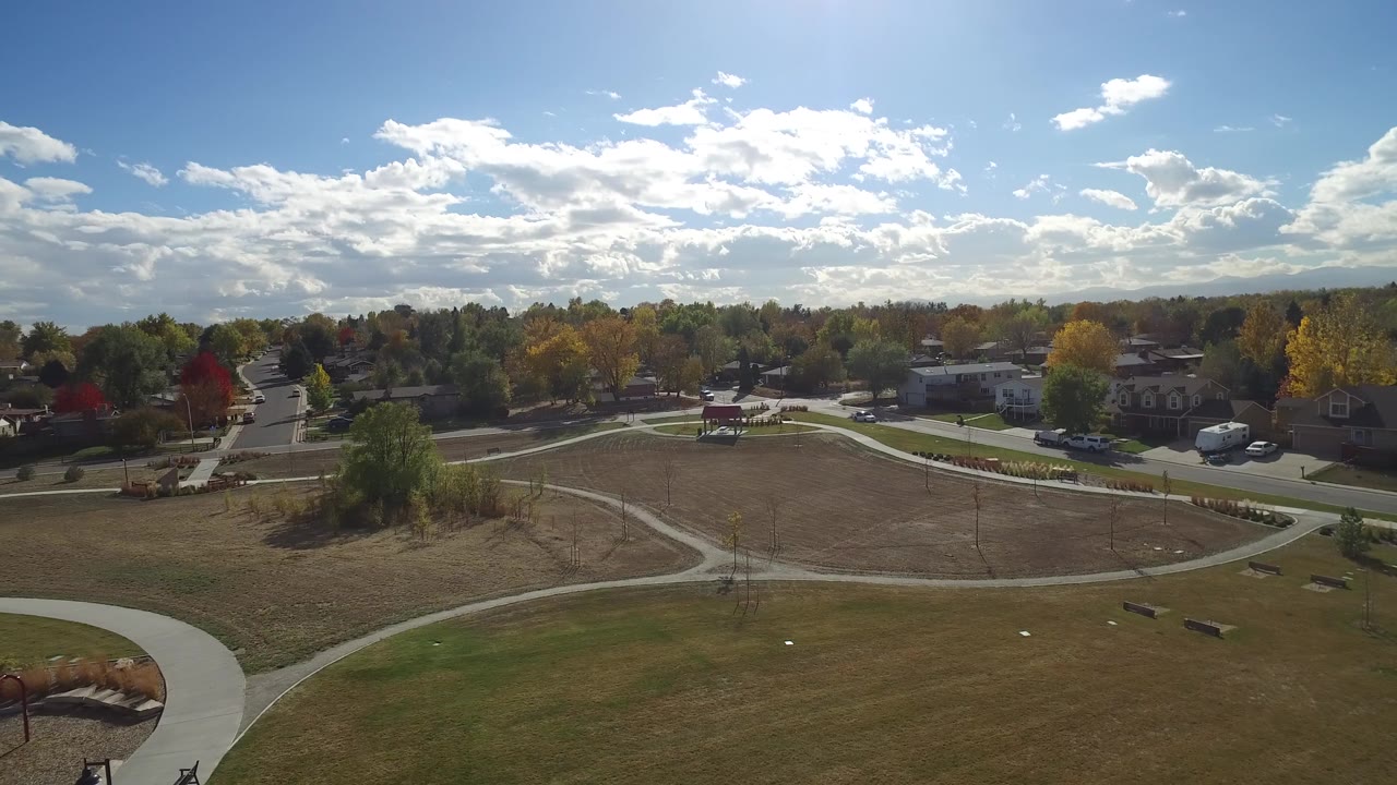 Aerial frame over Hidden Lake, Colorado, showing open park grass, intersecting sidewalks, benches, tree-lined streets, homes, and no visible people.