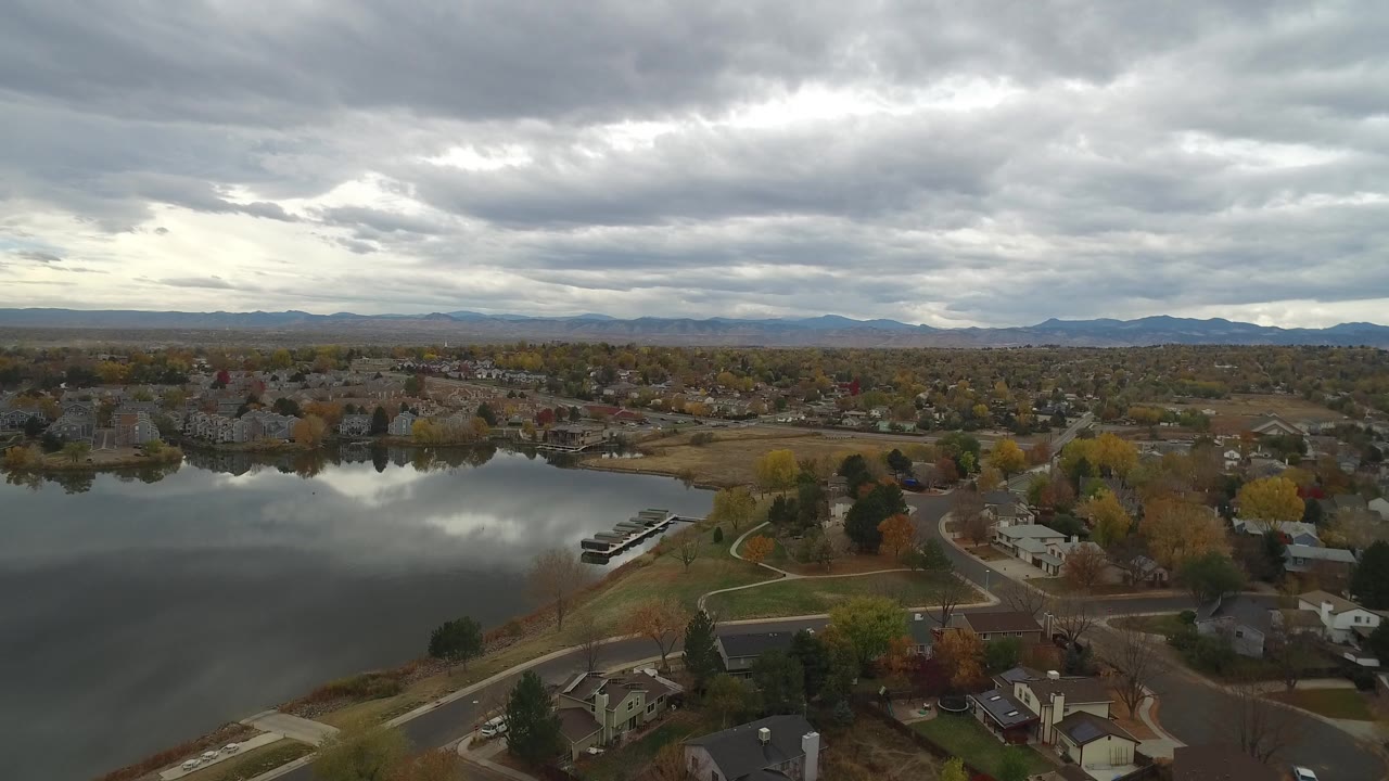 Wide aerial view of a suburban lake area with mountains beneath thick clouds.