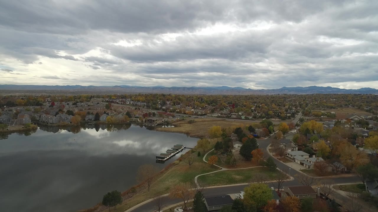 Wide aerial of lakeside houses, curving roads, docks, and gray clouds.