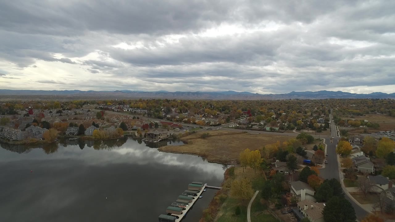 Aerial view over lake, docks, suburban homes, and cloudy sky.
