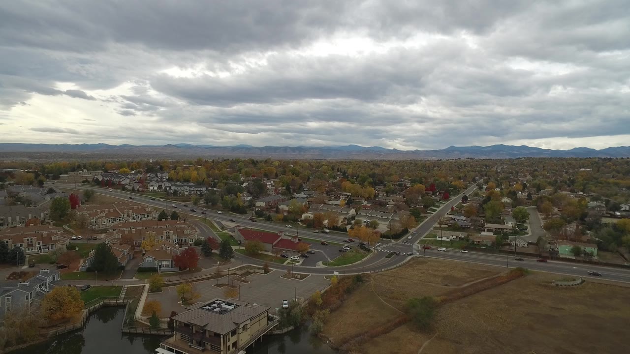Aerial view of suburban roads, homes, autumn trees, and cloudy sky.