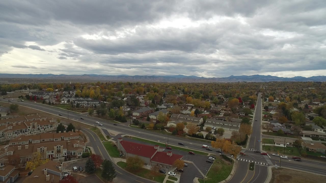 Aerial view of suburban homes, roads, trees, and cloudy sky.