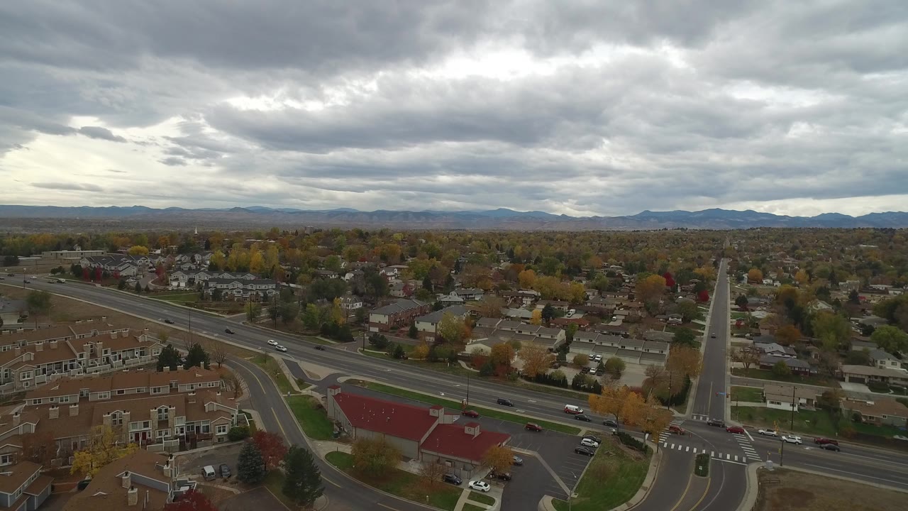 Hidden Lake, Colorado aerial view showing a tall pointed tower or monument near an intersection, houses, cars on the road, fall trees, mountains, and no clearly visible people.