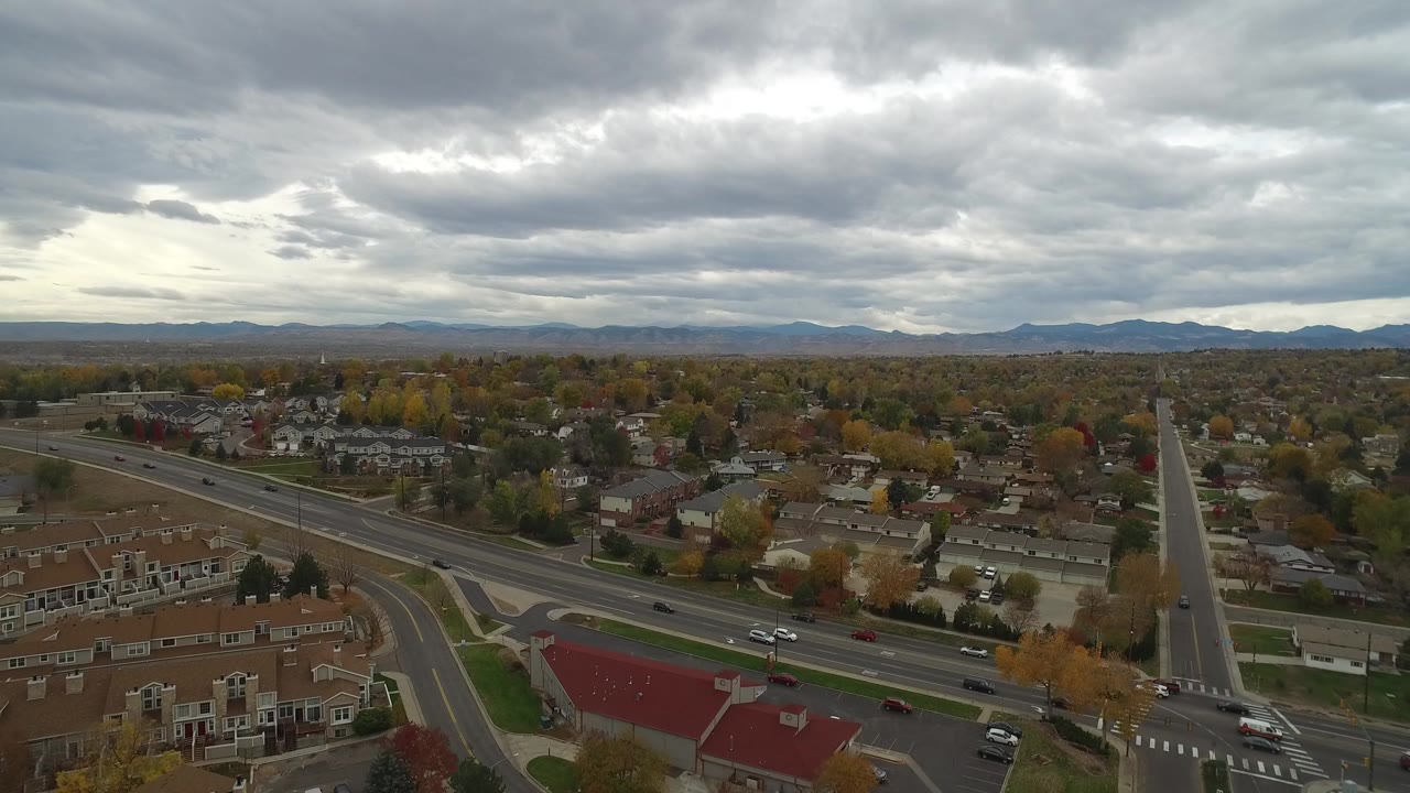 Aerial view of townhomes, roads, trees, and distant mountains under gray clouds.