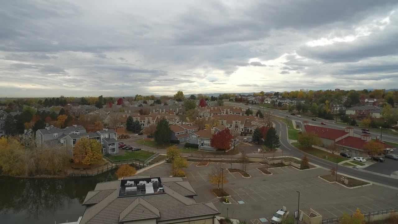 Aerial view in Hidden Lake, Colorado with the waterfront building lower in frame, docks along the water, neighborhood homes in the distance, muted fall color, and no visible people.
