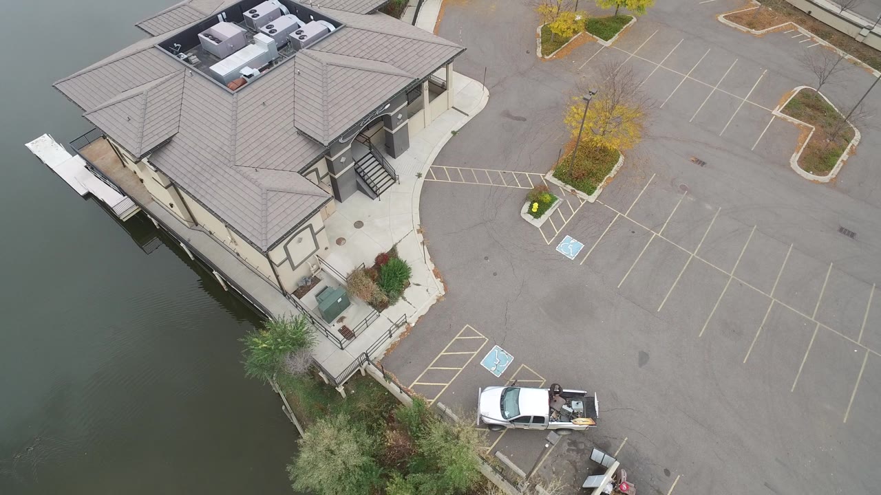 Second frame of the Hidden Lake, Colorado aerial shows the commercial roof, dockside water edge, marked spaces, a white pickup near the lower lot, and no visible people.