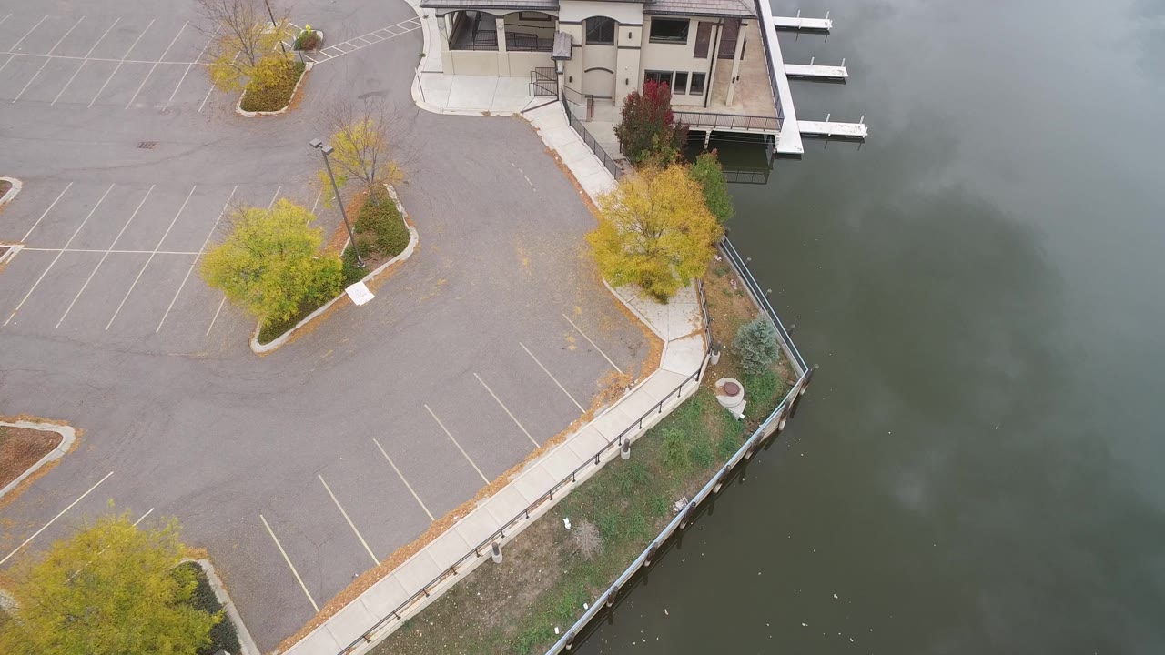 Top-down view of waterfront parking lot, trees, building, docks, and lake.