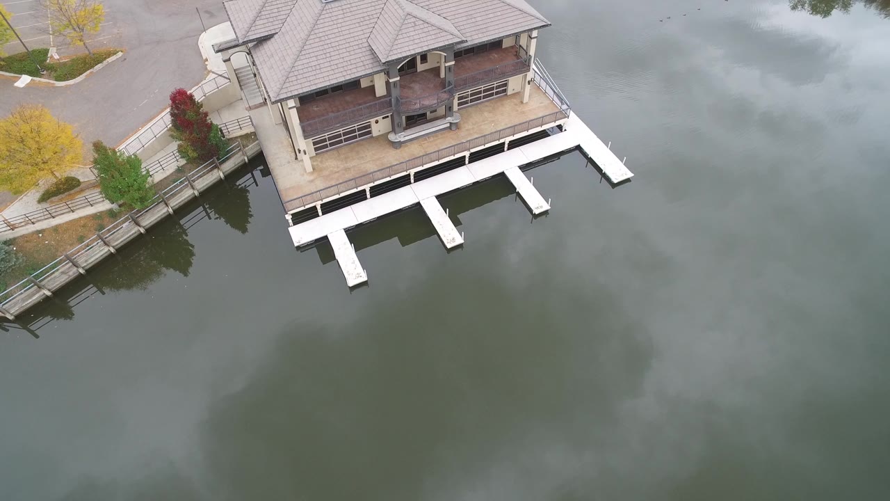 At 0:01, the drone view keeps the Hidden Lake house near the upper frame with dock slips below it, a fenced shoreline path to the left, and no visible people.