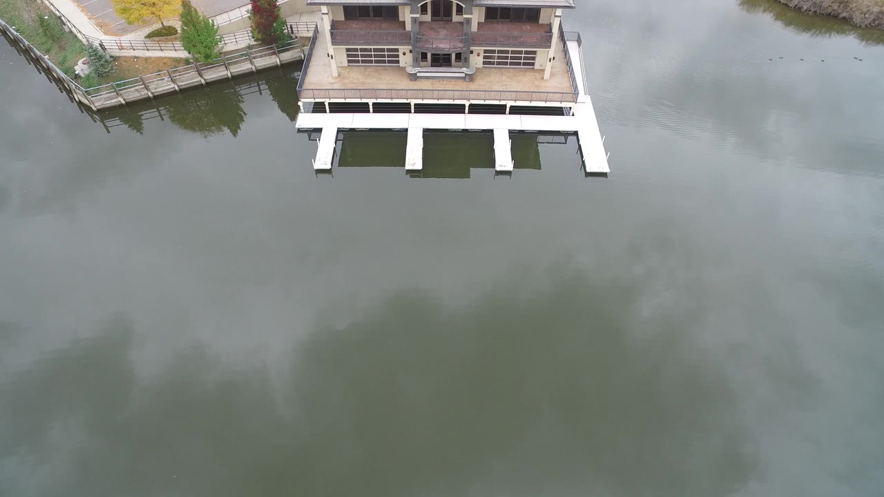 Aerial view of a lakeside home and white dock over green water.