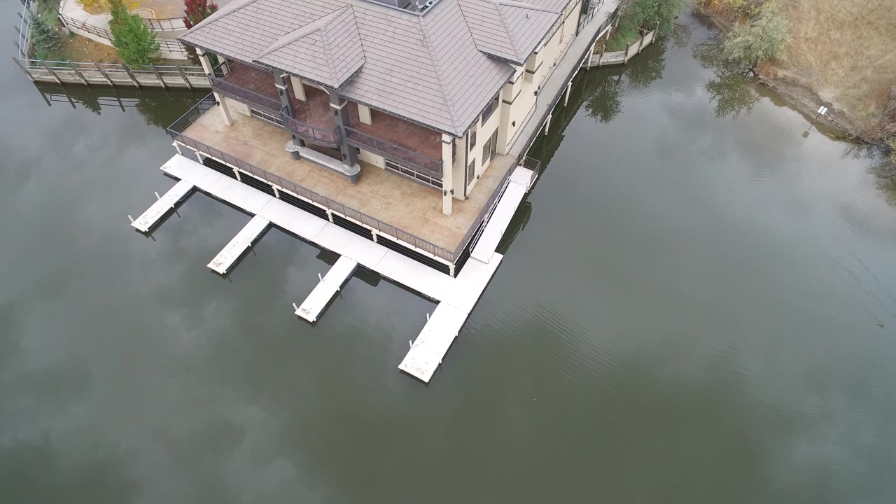 Overhead drone view of a lakeside house with white docks in green water.