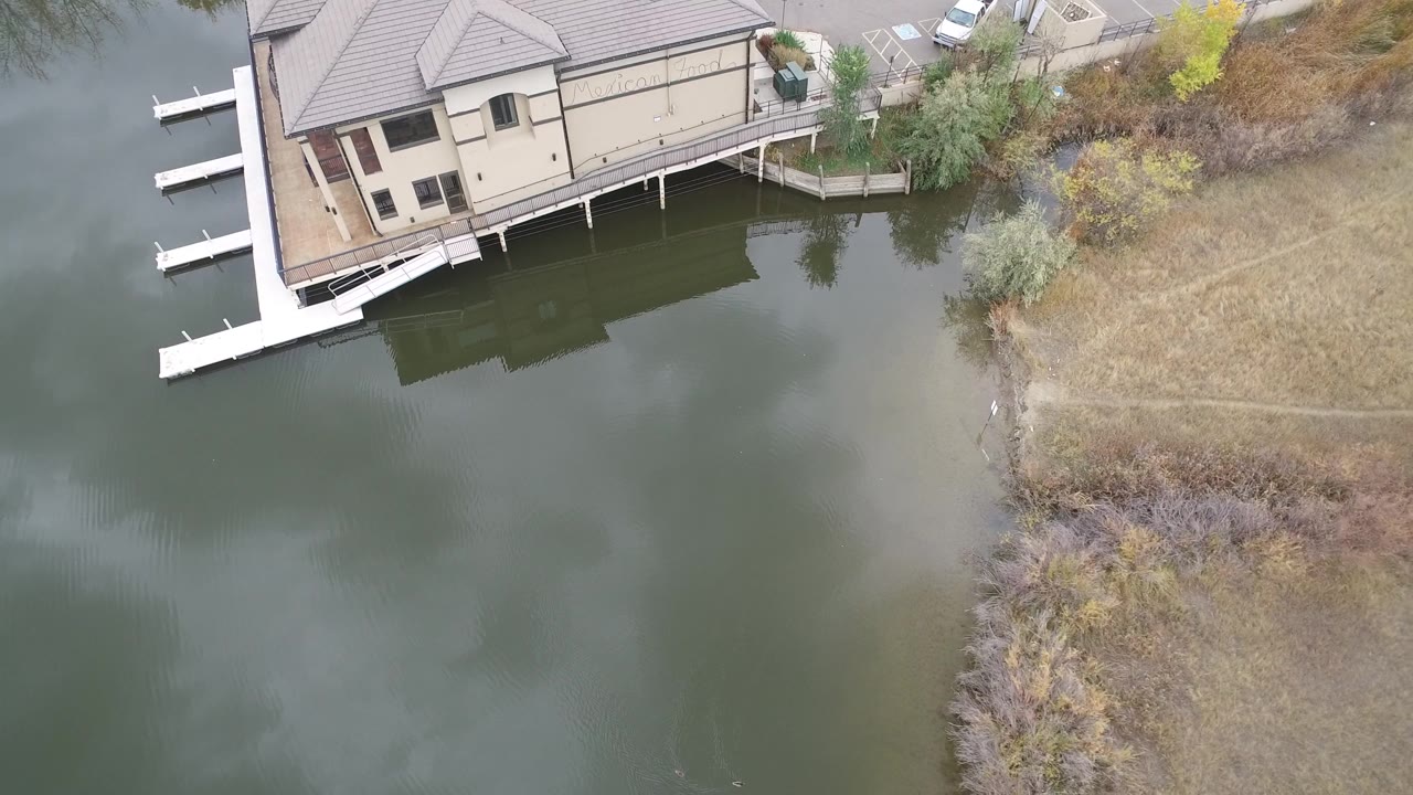 Top-down view of a large house beside water with white docks and a shoreline path.