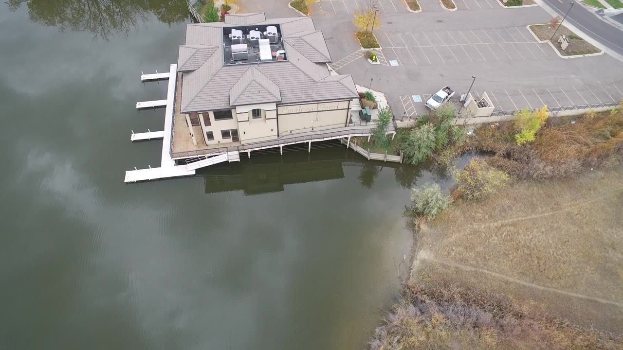 Aerial view of a lakeside house, docks, parking lot, and shoreline.