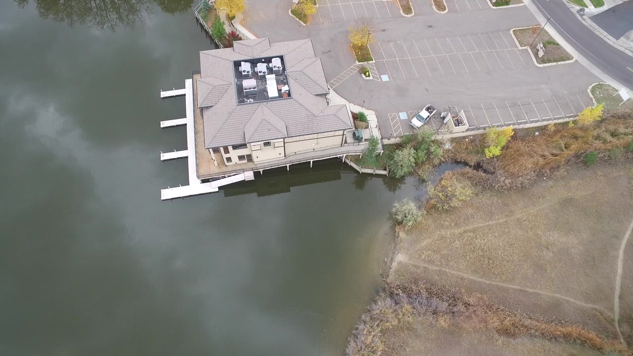 Overhead view of a lakeside building, docks, water, parking lot, and dry shoreline ground.