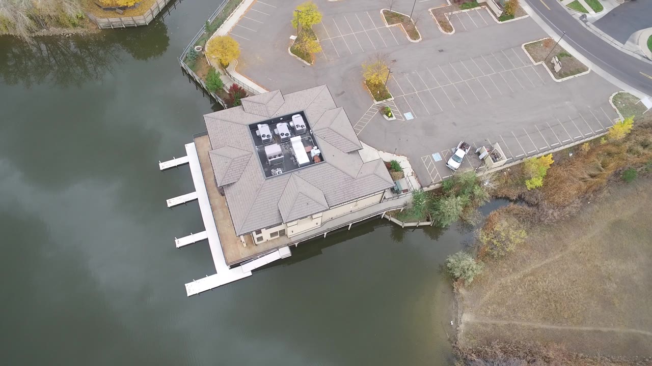 Hidden Lake, Colorado frame showing the waterfront building slightly lower in view, with white docks projecting into the lake, a mostly empty parking lot, autumn trees, and no visible people.