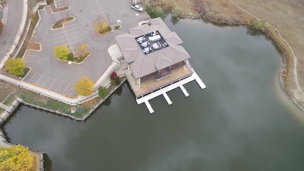 Overhead frame in Hidden Lake, Colorado showing a roofed lakeside building, white dock fingers, nearby parking spaces, muted water, and no visible people.
