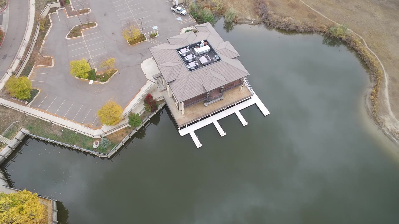 Aerial frame in Hidden Lake, Colorado with the lakeside building near center, dock slips on the water side, empty parking stalls to the left, and no visible people.