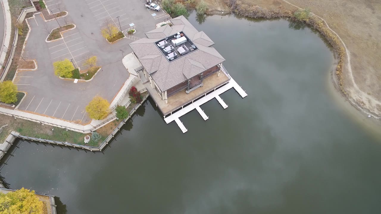 Drone-like overhead view of a building beside a lake with docks and parking bays.