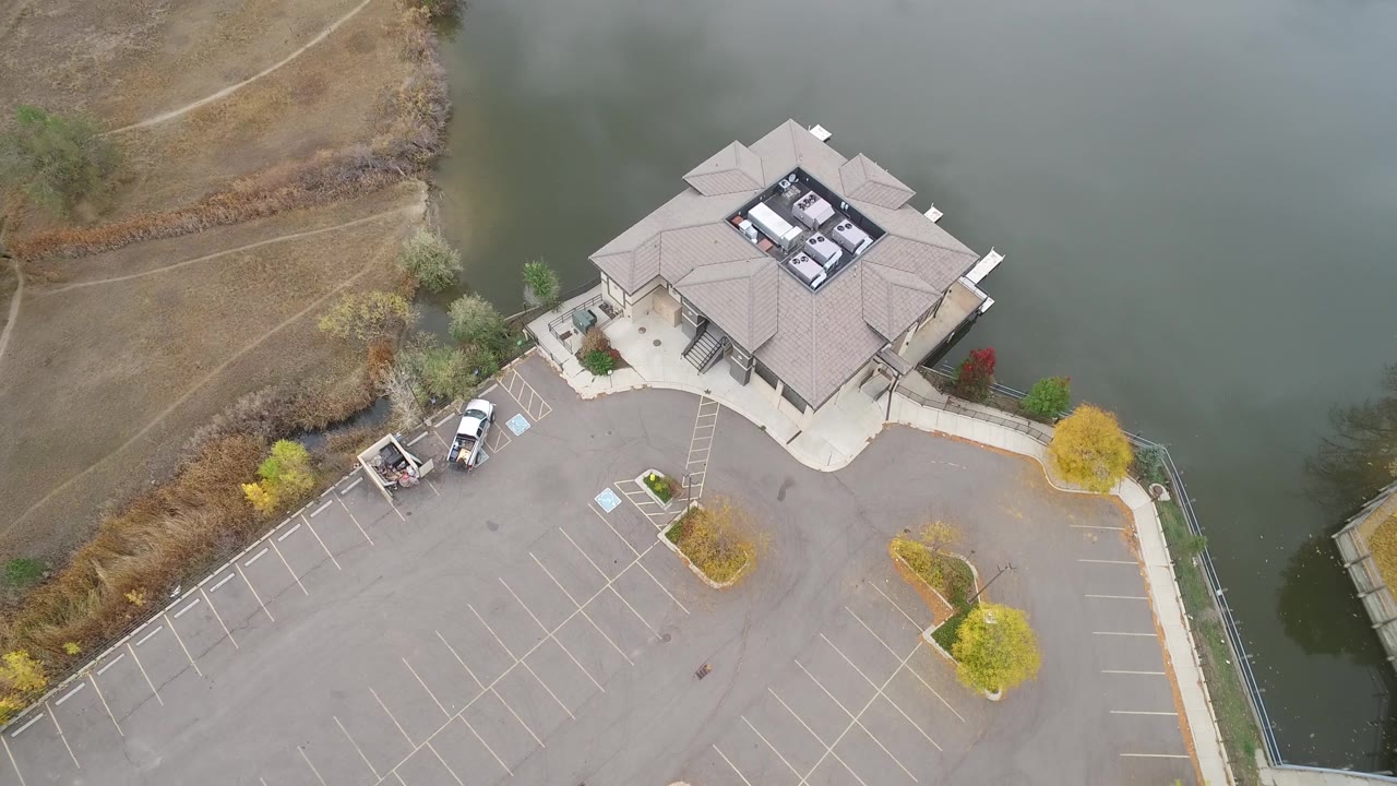 High aerial view of a roofed building on the edge of a lake with parking spaces below.