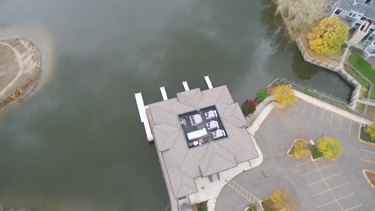 A second overhead frame in Hidden Lake, Colorado keeps the lakeside building near the lower center, with dock slips to the left, parking spaces to the right, green water around it, and no visible people.