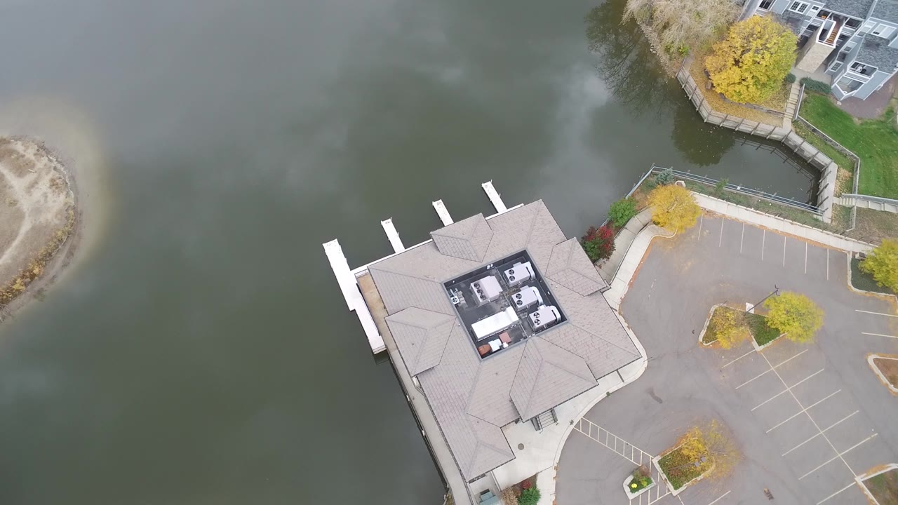 Drone view of the lakeside building, docks, road edge, and empty parking area.