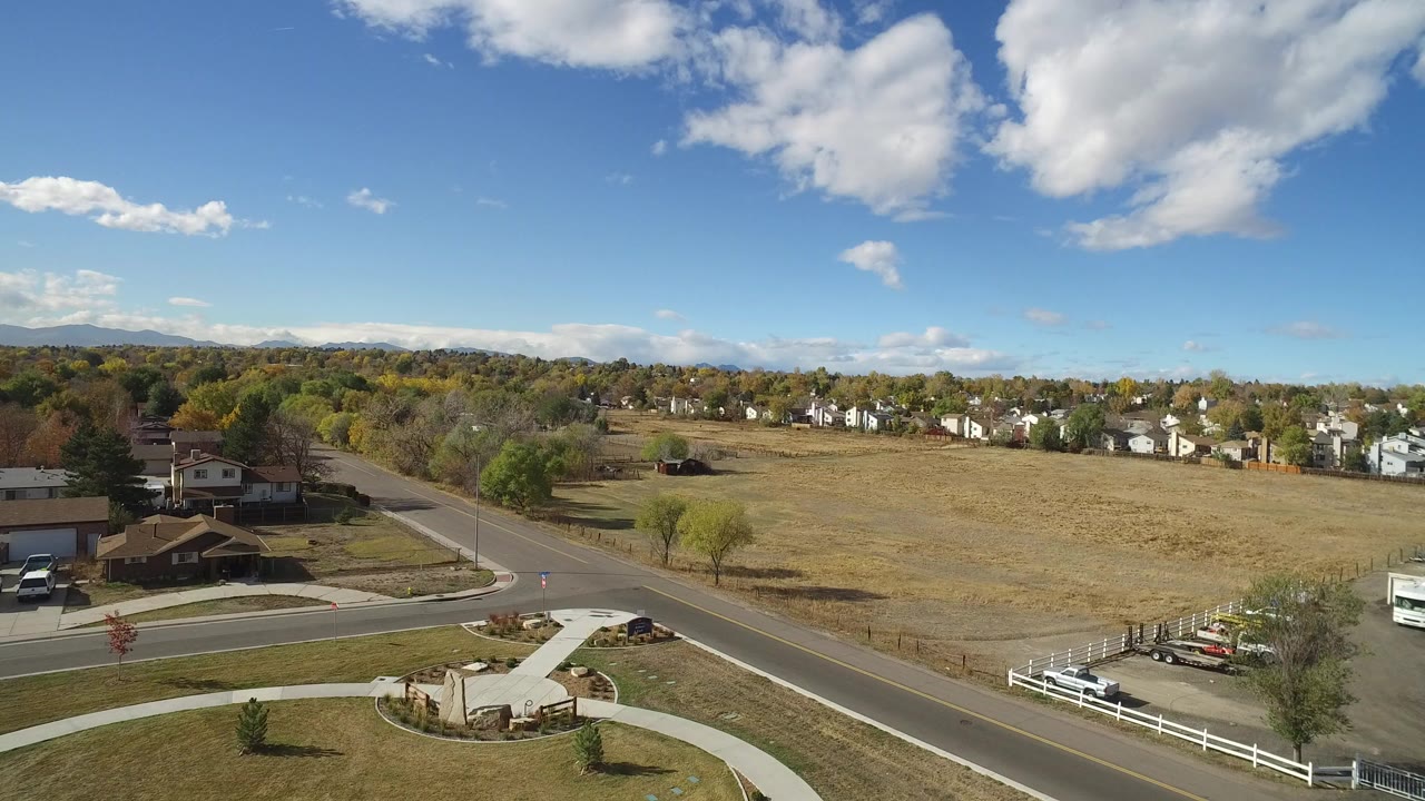 Aerial view of roads, open field, houses, trees, and distant hills under clouds.