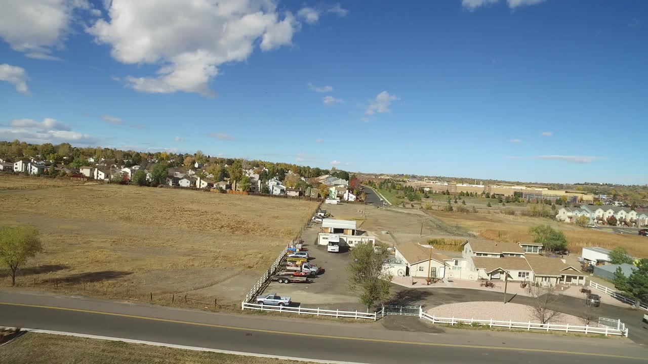 Hidden Lake, Colorado appears from an elevated angle with a parking area, several cars, low buildings, a road along the bottom of frame, open land behind, and no clearly visible people.