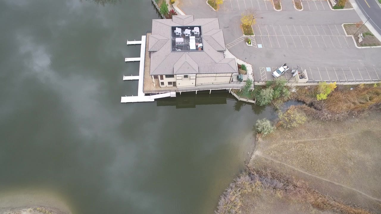 Overhead view of a lakeside building, docks, water, and an empty parking lot.