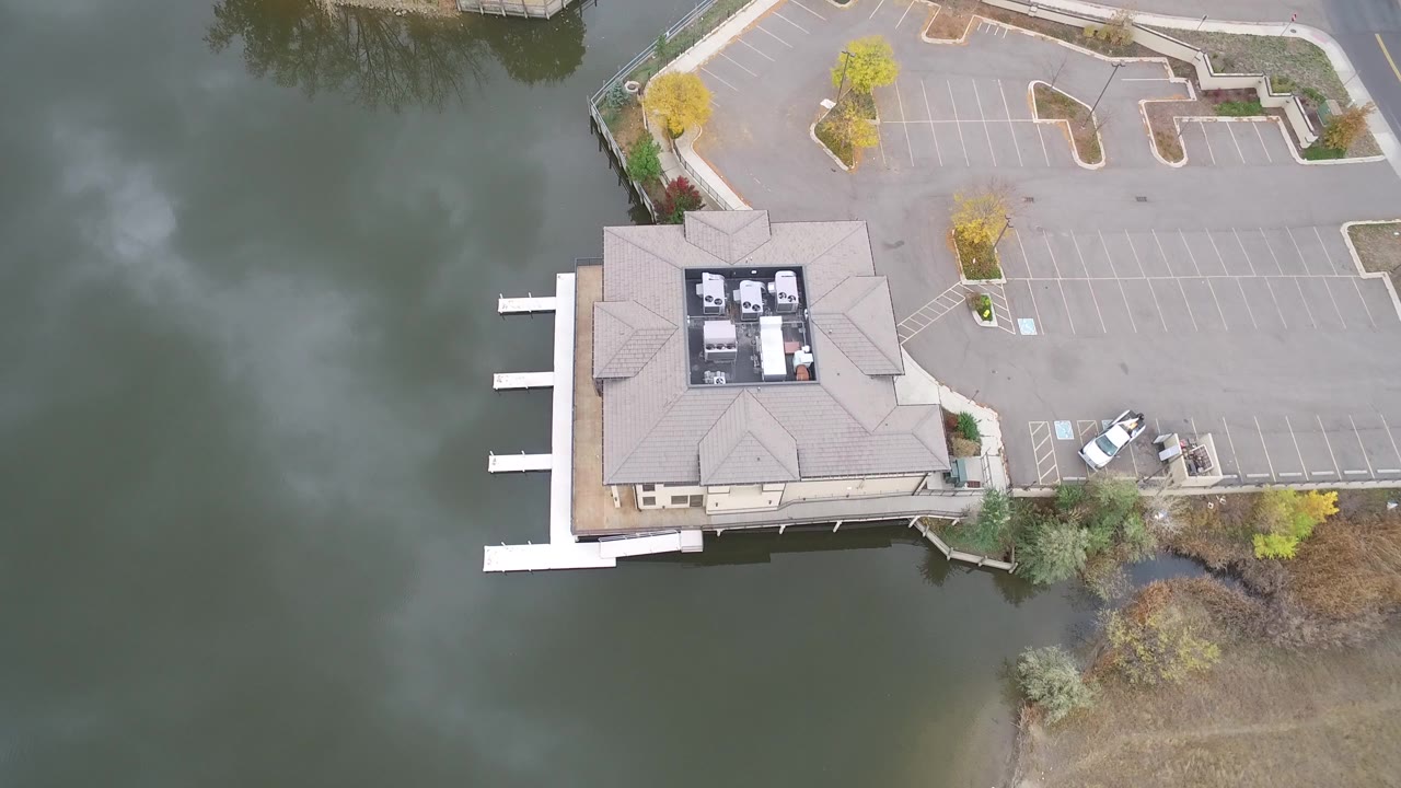 Overhead view of lake water, a docked lakeside building, and an empty parking lot.