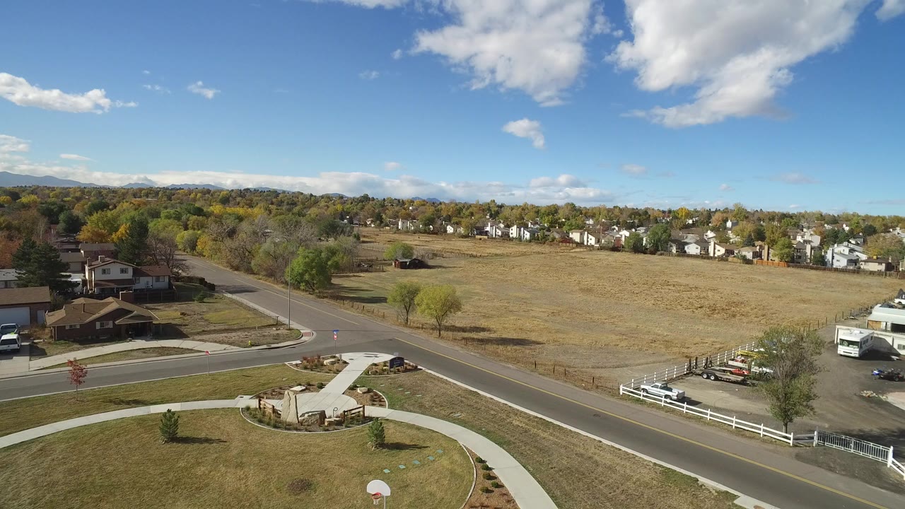 Aerial view of a road beside an open field and houses under a blue sky.