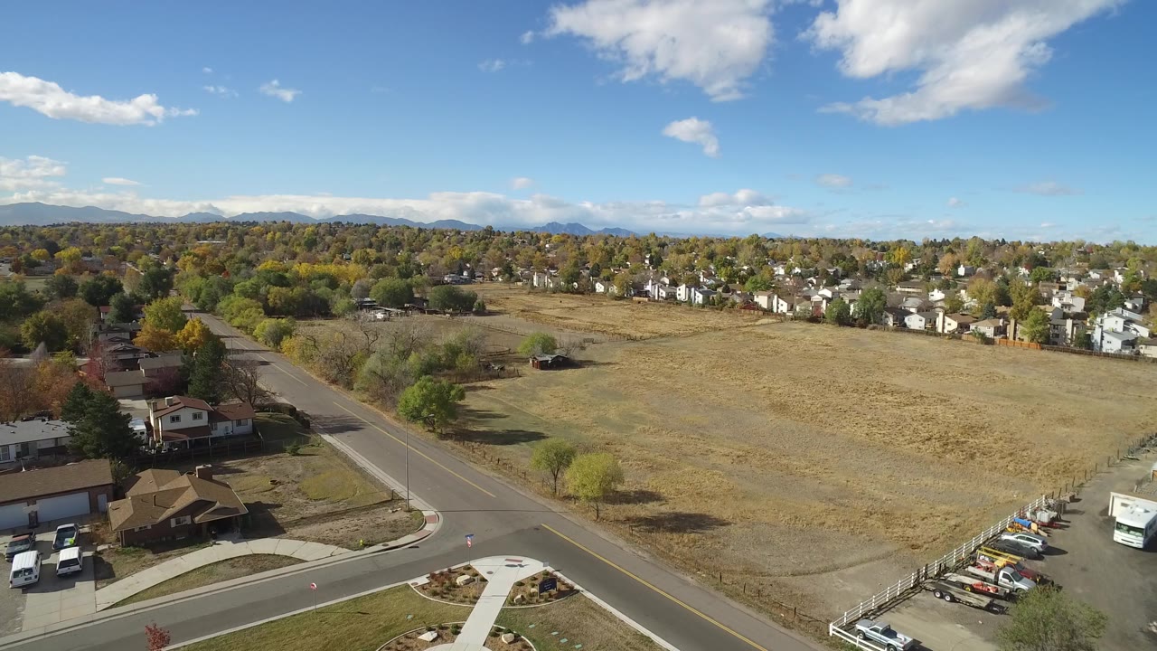 Drone-height view of suburban homes around a large field under blue sky.