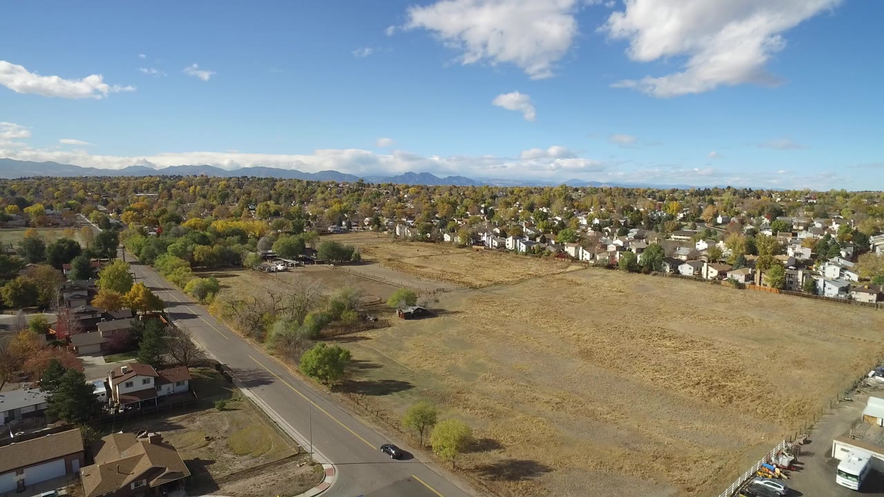 Aerial view of a road, open field, homes, trees, and distant mountains under blue sky.