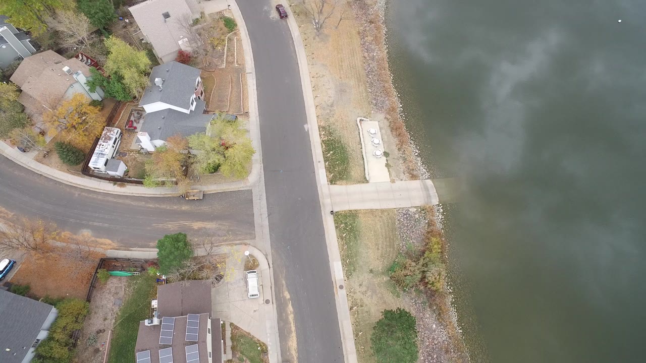High aerial frame over Hidden Lake, Colorado showing private homes, curved streets, a shoreline road, and green lake water with no visible people.
